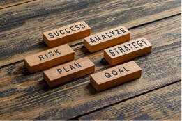 Building blocks on a table with the words on them: Success, Risk, Analyze, Plan, Strategy, Goal
